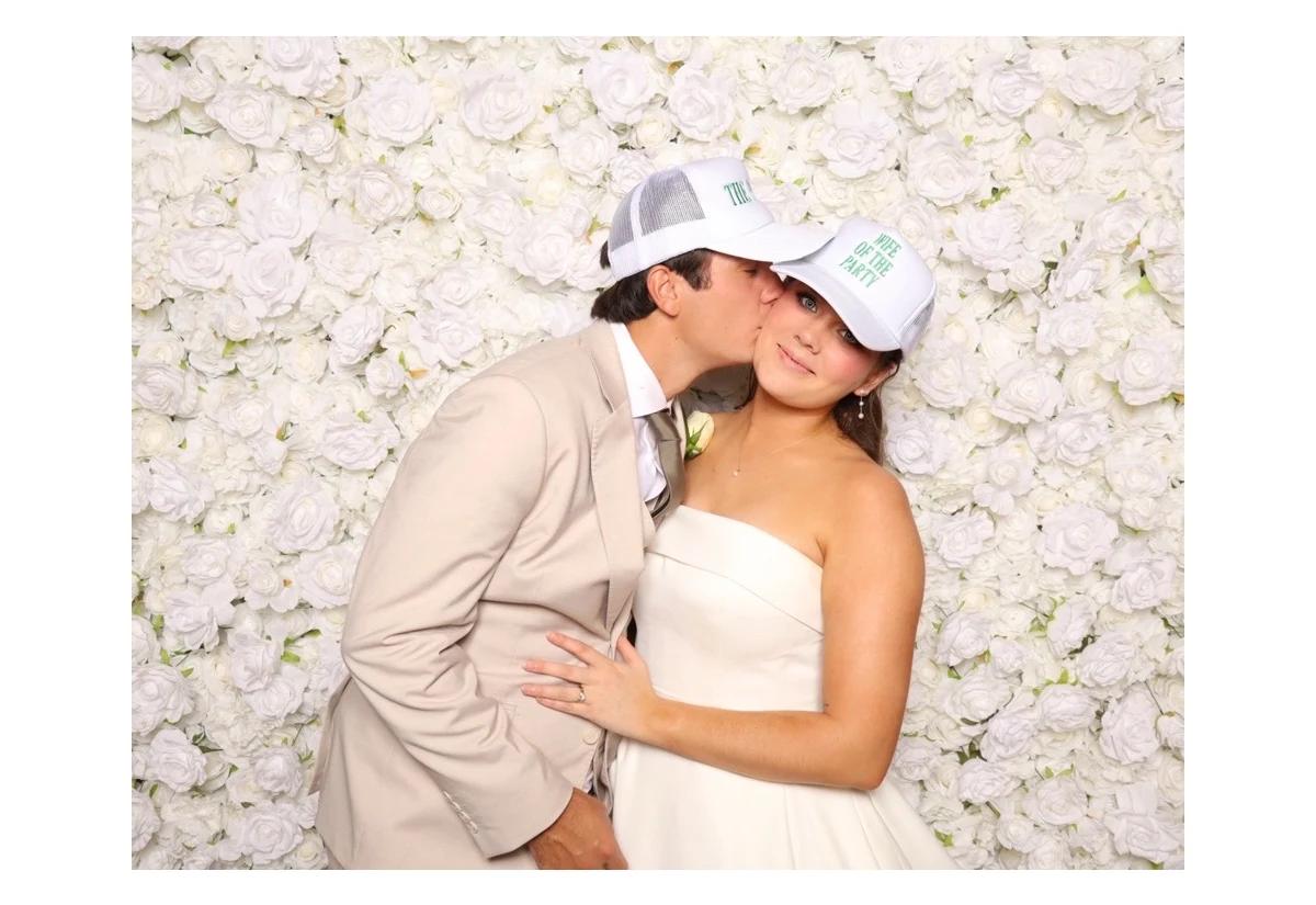 A couple kissing in front of the white flower wall, from one of the booth prints.