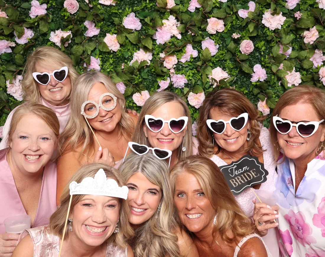 Guests holding photo booth props in front of a flower wall.