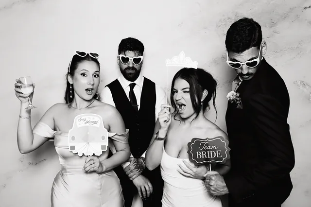 Two couples in a black and white booth photo with Just Married and Team Bride props.